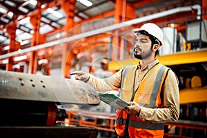 Men industrial engineer wearing a white helmet while standing in a heavy industrial factory behind. The Maintenance looking of