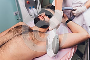 Men lying at beautician& x27;s during laser armpit hair removal therapy.