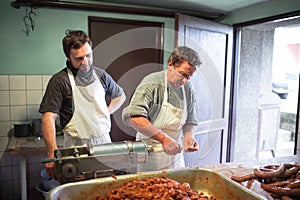 Men making sausages the traditional way using sausage filler.