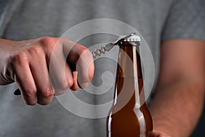 Men opening cold bottle of beer with cap on black background. Hands cracking refrigerated wheat or lager beer with an opener on