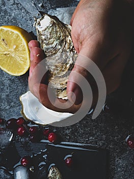 Men opening raw oyster with knife, closeup. The persons hands shucking fresh oysters
