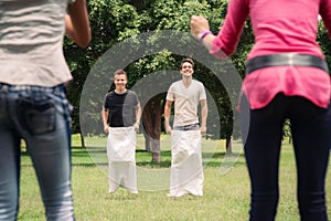 Men playing sack race with girlfriends cheering