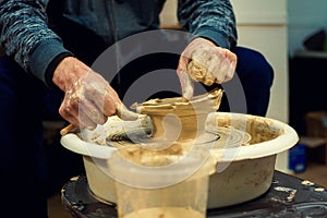 The men potters hands form by a clay pot on a potters wheel. The potter works in a workshop.