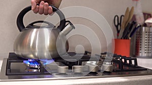 Men puts the kettle on the stove. He turns on the stove and puts the kettle with water on the fire. The flame is blue.