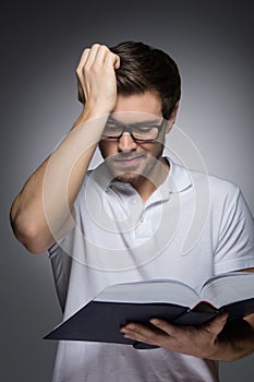 Men reading a book. Portrait of young men reading a book and holding his hand in hair while standing isolated on grey