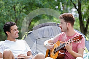 men relaxing by tent one playing guitar