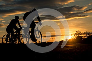The men ride bikes at sunset with orange-blue sky background. photo