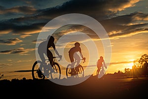 The men ride bikes at sunset with orange-blue sky background. photo