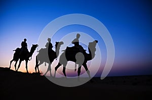 Men Riding Camel Through The Dimly Lit Desert