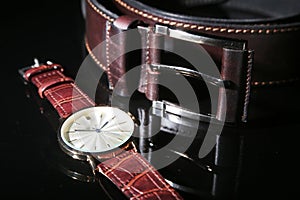 Men`s accessories for business and rekreation. Leather belt, Watch, notepad and pen on black mirror background. Top view