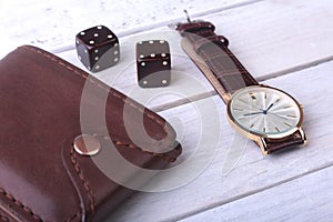 Men`s accessories for business and rekreation. Watch, leather wallet and dice on wood background.. Top view composition.