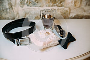 Men`s accessories, leather belt, perfume, bow tie, groom`s golden rings, watches and brides on a white table