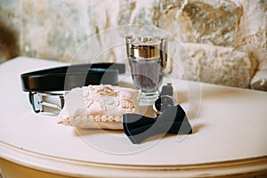 Men`s accessories, leather belt, perfume, bow tie, groom`s golden rings, watches and brides on a white table