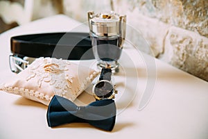 Men`s accessories, leather belt, perfume, bow tie, groom`s golden rings, watches and brides on a white table