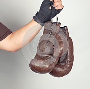 men's arm wrapped in a black elastic sports bandage holds pair old vintage leather boxing gloves