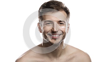 Men's beauty. Young man is applying moisturizing and anti aging cream on his face