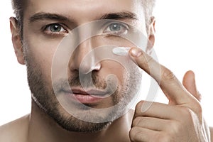 Men's beauty. Young man is applying moisturizing and anti aging cream on his face