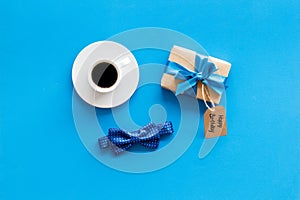 Men`s birthday concept. Happy birthday text, present box, bow tie and coffee on blue background top view