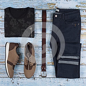 Men`s casual outfits. Men shoes, clothing and accessories on wooden background - t-shirt, jeans, sneaker, belt. Top view. Flat la