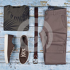 Men`s casual outfits. Men shoes, clothing and accessories on wooden background - t-shirt, jeans, sneaker, belt. Top view. Flat la