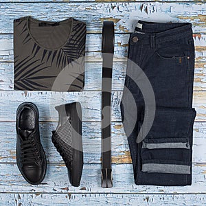 Men`s casual outfits. Men shoes, clothing and accessories on wooden background - t-shirt, jeans, sneaker, belt. Top view. Flat la