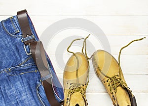 Men`s casual wear, yellow work boots from natural nubuck leather, blue jeans and brown belt on wooden white background top view
