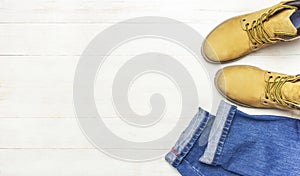 Men`s casual wear, yellow work boots from natural nubuck leather, blue jeans and brown belt on wooden white background top view