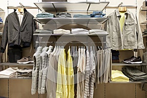 Men\'s clothing on hangers in a boutique grouped by color. Jackets, trousers and shoes.