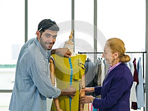 Men`s dressmaker measuring length of green dress from neck to waist from a mannequins