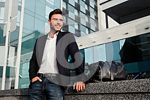 Men`s fashion. A young male businessman in a trendy suit and a white shirt with a big black handbag comes out from a fashionable