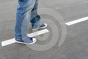 Men`s feet on the asphalt. A man walks along the road markings