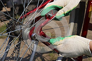 Men`s gloved hands repair the back wheel of the bike, close-up. A man repairs a vintage bicycle outdoors with tools. DIY concept