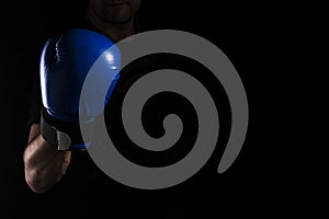 Men`s hand in a blue boxing glove on a black background makes a punch - hook