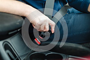 Men`s hand fastens the seat belt of the car.