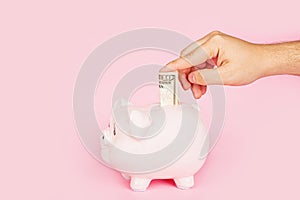 Men`s hand holding cash money in Piggy bank on pink background. mockup, template. Banner with copy space. Concept of savings mone