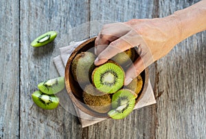 Men`s hand holding fresh kiwi fruit in the bowl on wooden background