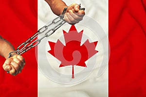 Men`s hands chained in heavy iron chains against the background of the flag of Canada on a gentle silk with folds in the wind, th