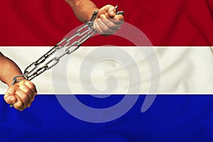 Men`s hands chained in heavy iron chains against the background of the flag of Holland on gentle silk with folds in the wind,