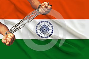 Men`s hands chained in heavy iron chains against the background of the flag of India on a gentle silk with folds in the wind, the