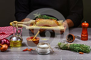 Men`s hands, close-up, holding meat steak, herbs and spices on wooden table, home cooking concept