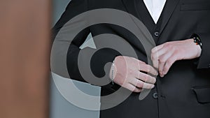 Men's hands fasten buttons on a suit jacket. Close up