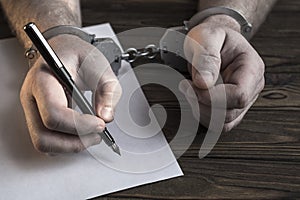 Men`s hands with handcuffs fill the police record, confession.
