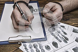 Men`s hands with handcuffs fill the police record, confession.