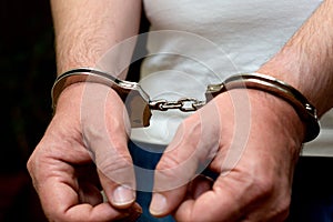 Men`s hands in handcuffs. A man in a white T-shirt in handcuffs. Close-up