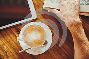 Men's hands hold coffee and book on the table