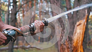 Men`s Hands Hold a Fire Hose from Which Water Runs under Pressure in Pine Forest