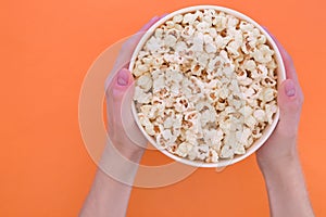 Men`s hands hold a paper cup with popcorn on an orange background. Man with popcorn in his hands.solated