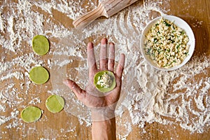 Men`s hands holding a blank for vegetable dumplings. Preparation of meat dumplings on the wooden table.