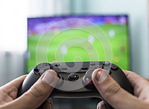 Men`s hands with a joystick on the background of a TV, playing football, close-up