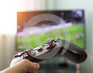 Men`s hands with a joystick on the background of a TV, playing football, close-up